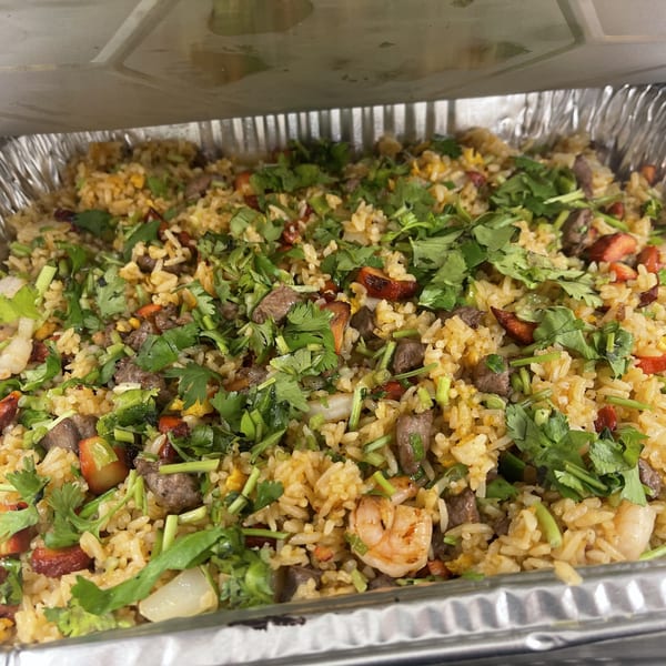Close-up of a large catering tray filled with colorful fried rice, topped with cilantro.