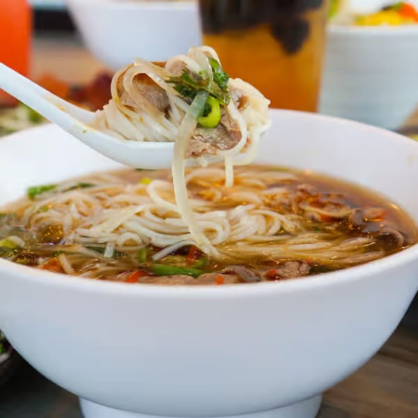 A spoonful of pho noodles and beef being lifted from a white bowl of broth.