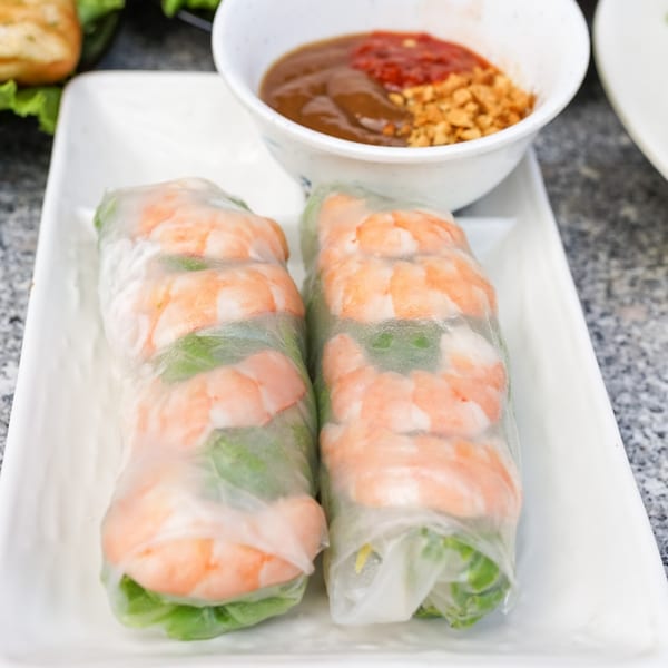 Two fresh Vietnamese shrimp spring rolls with peanut sauce and chili sauce on a white plate.