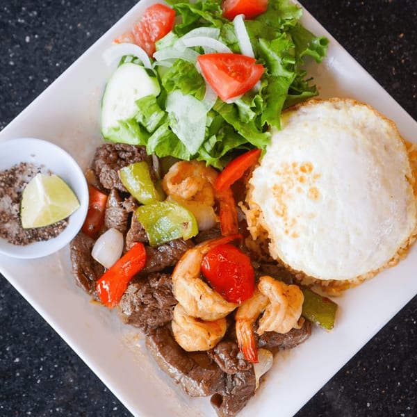 Vietnamese dish with stir-fried beef and shrimp, fried egg, rice, and a side salad.