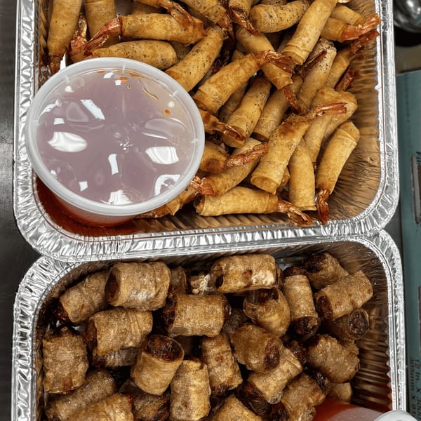 Two foil trays of fried spring rolls, one with shrimp and a dipping sauce, the other with meat.
