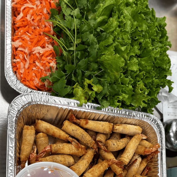 Two foil trays filled with fresh lettuce, cilantro, shredded carrots, and crispy shrimp spring rolls.
