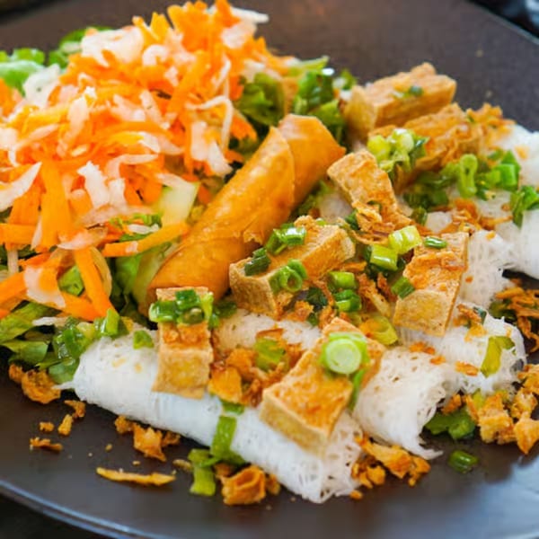 Vietnamese dish with spring rolls, tofu, shredded carrots, and greens on a dark plate.