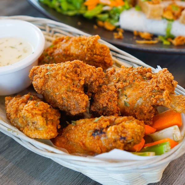 Crispy fried chicken wings with a side of dipping sauce and pickled vegetables in a basket.